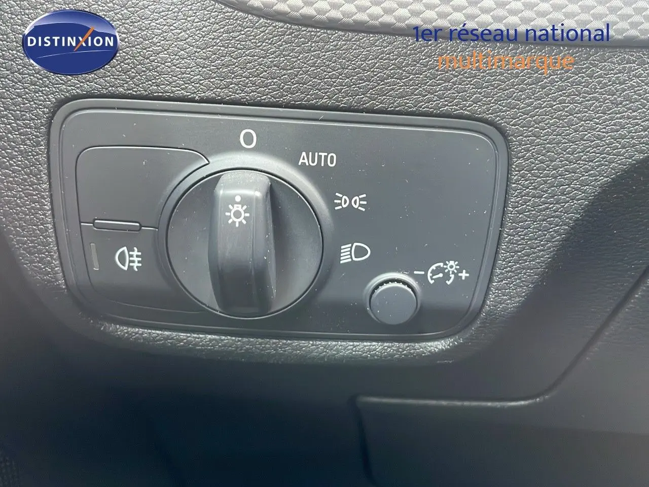 Gros plan sur le bouton de commande des phares de l'Audi Q2 noir mito metal, avec réglage automatique et options éclairage.