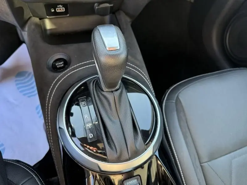 Le levier de vitesse automatique noir du Nissan Juke 1.6 Hybrid 2024, avec coutures blanches et bouton start/stop visible.