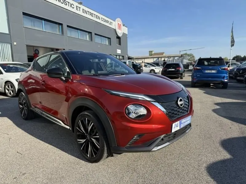 Nissan Juke 1.6 Hybrid 143ch N-Design rouge Fuji métal avec toit noir, vue 3/4 avant droit sur parking.