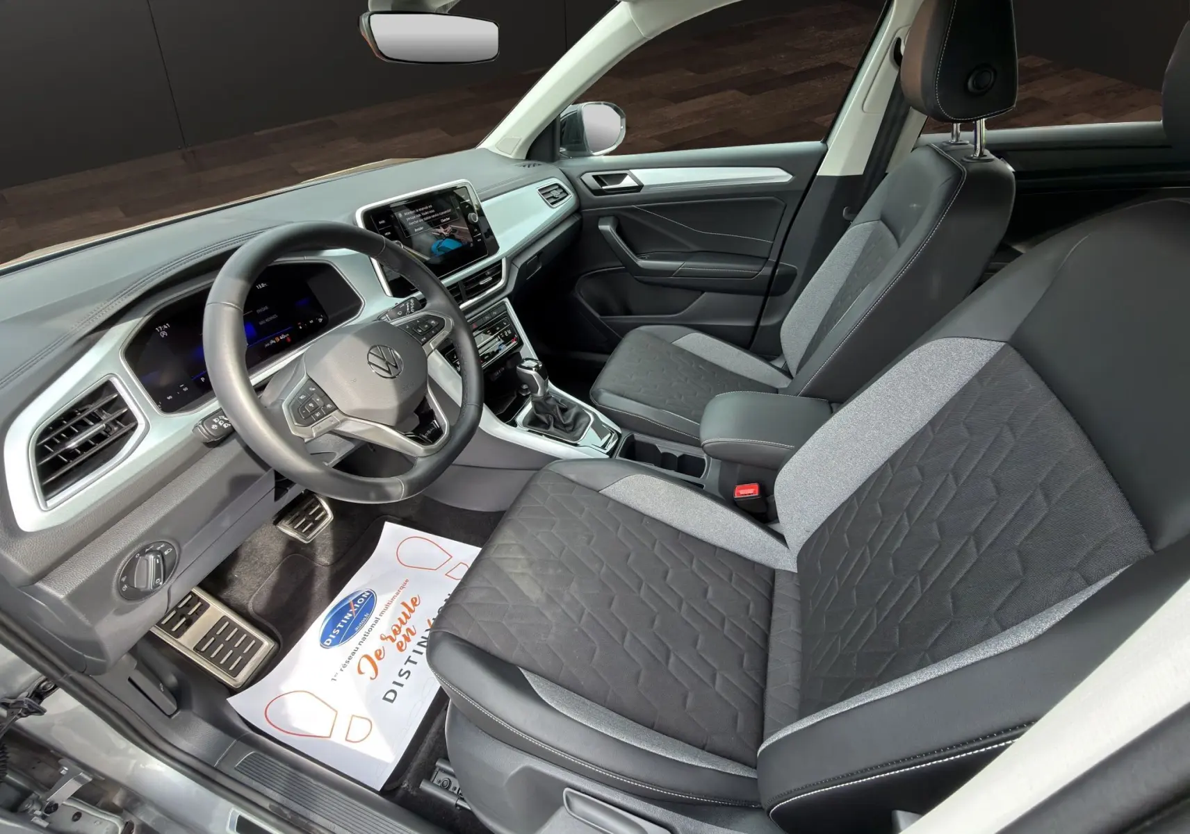 Vue intérieure côté conducteur du Volkswagen T-Roc 2025 avec sièges bi-matière gris et noir et tableau de bord moderne.