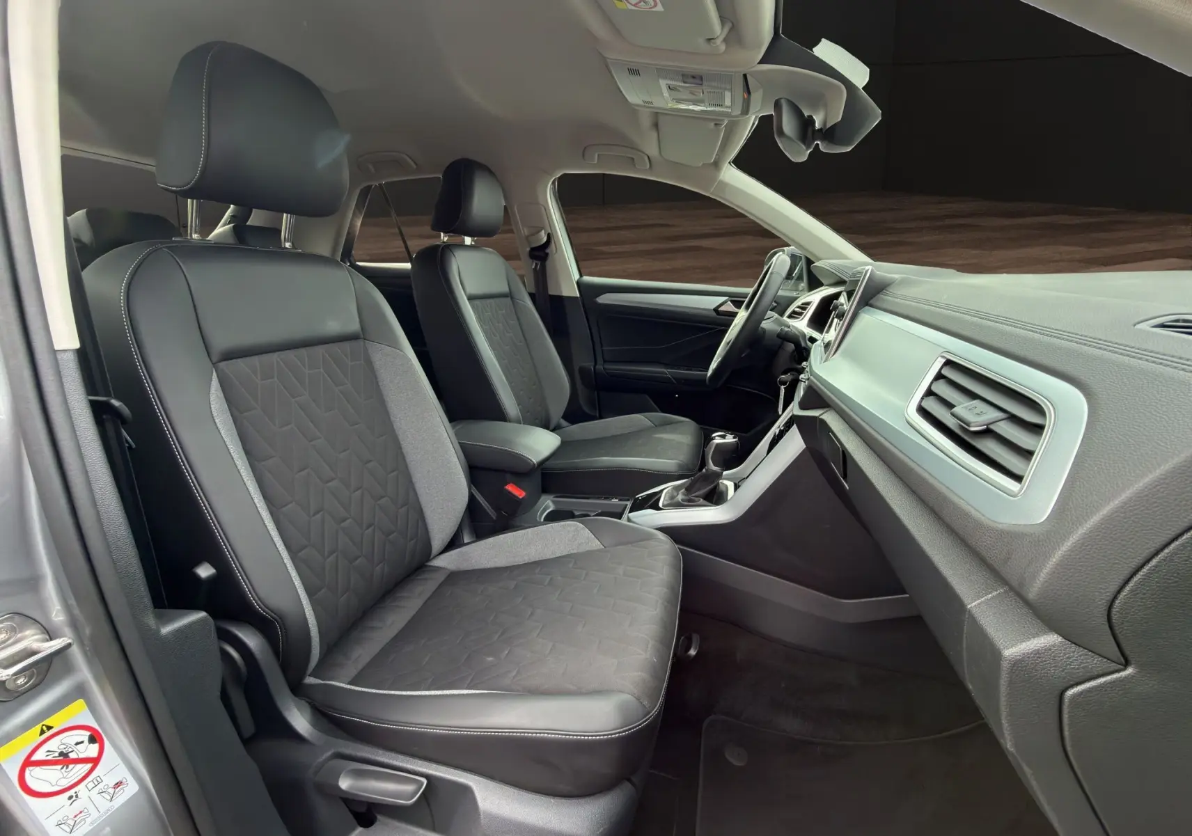 Vue intérieure côté gauche du Volkswagen T-Roc 2025, sièges tissu et cuir noirs avec console centrale et tableau de bord gris.