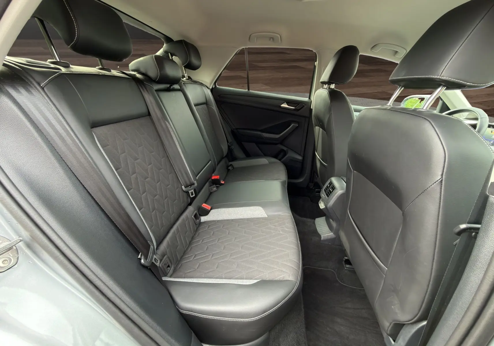 Vue intérieure arrière du Volkswagen T-Roc 2025, sièges noirs en cuir et tissu avec ceinture de sécurité visible.