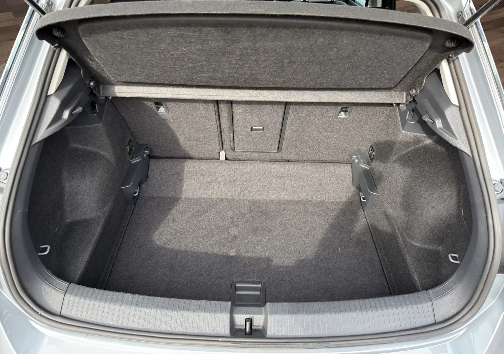 Vue plongeante sur le coffre ouvert du Volkswagen T-Roc gris Pyrite, montrant l’espace de rangement et la tablette cache-bagages.