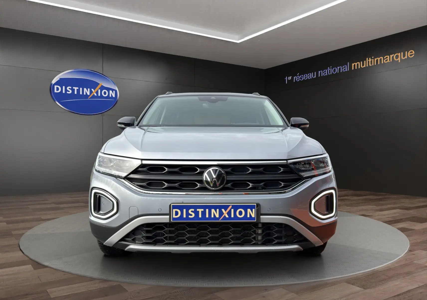 Vue frontale du Volkswagen T-Roc gris Pyrite avec calandre noire et feux LED en forme de C allumés.