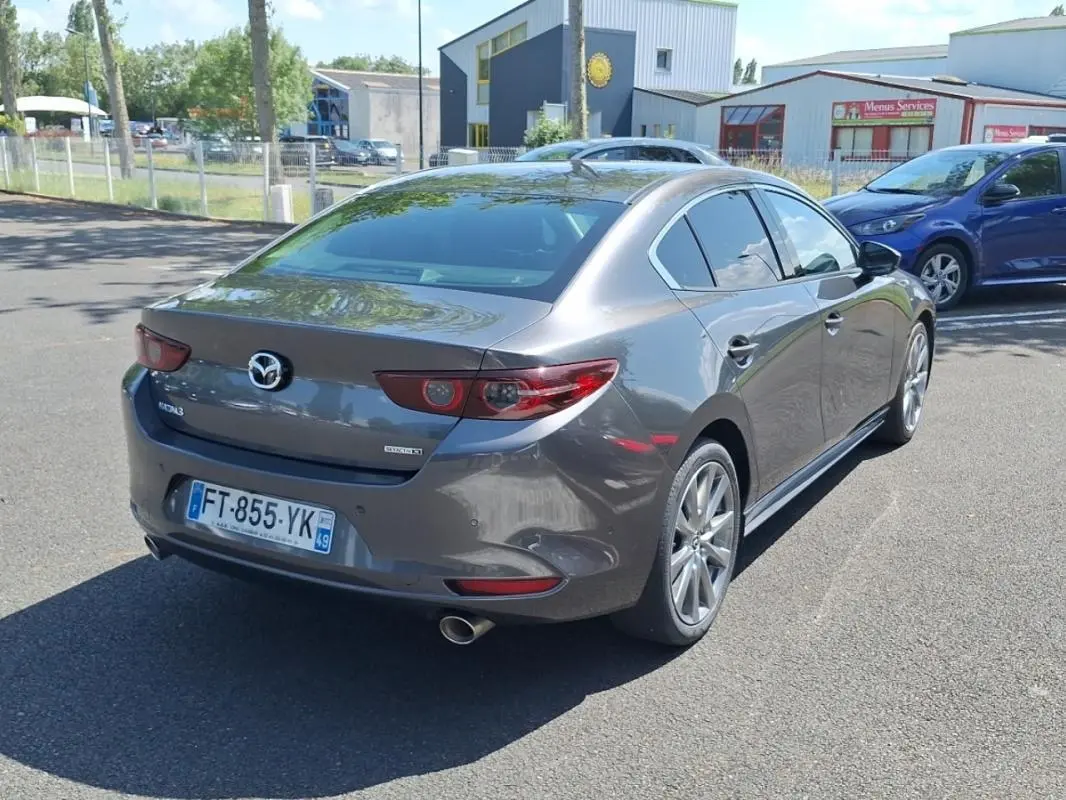 Vue 3/4 arrière droite d'une Mazda3 gris métallisé avec jantes aluminium et feux arrière LED distinctifs.