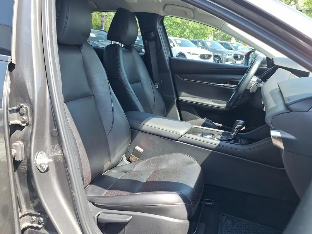 Vue intérieure côté conducteur de la Mazda3 gris, montrant sièges cuir noirs et console centrale avec levier de vitesse.