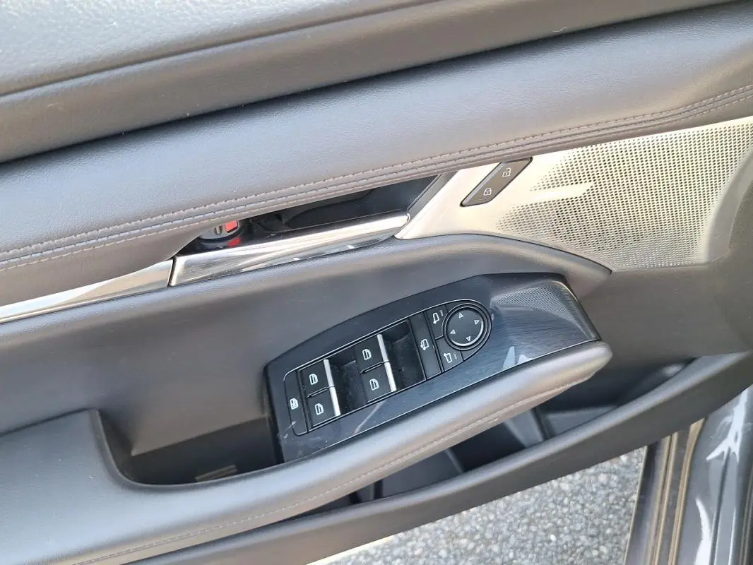 Gros plan sur la commande des vitres électriques et rétroviseurs sur la porte avant gauche grise d'une Mazda3.