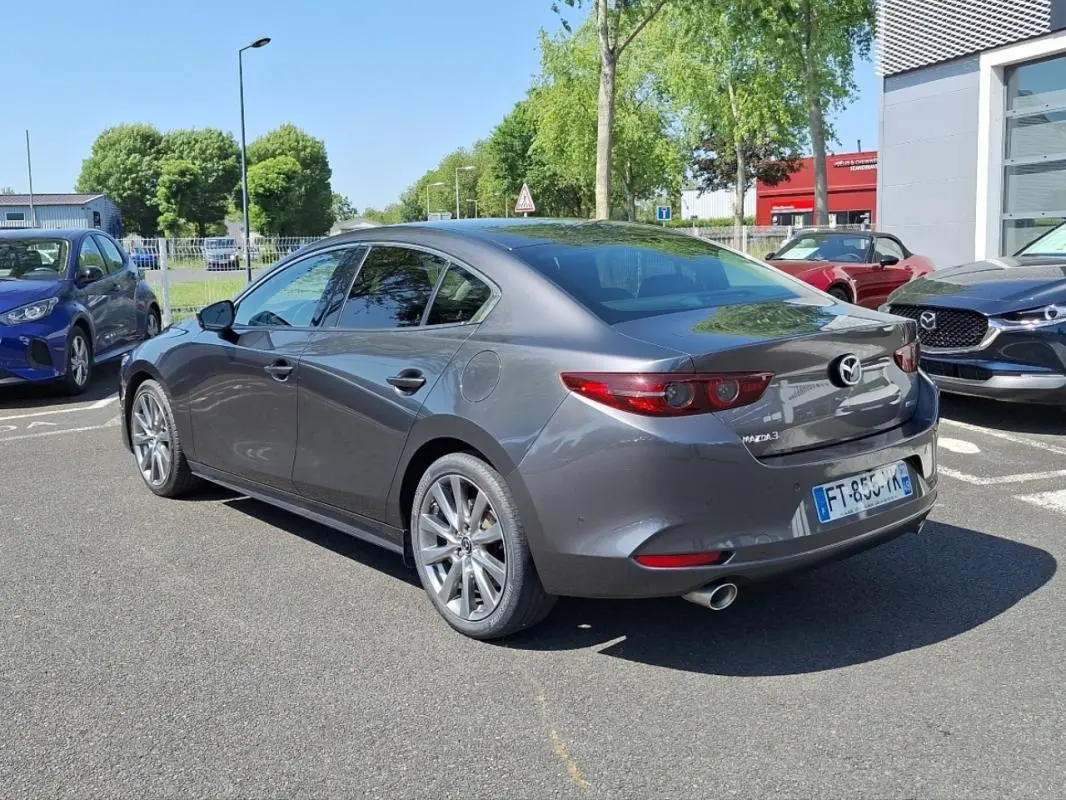 Vue 3/4 arrière droite d'une Mazda3 gris métallisé 2020 avec jantes aluminium et feux arrière LED distinctifs.