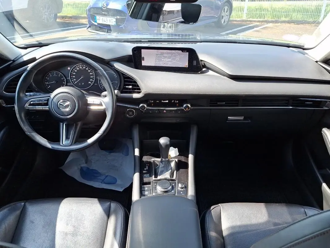 Vue intérieure avant de la Mazda3 2020 gris, mettant en valeur le volant cuir multifonctions et l’écran GPS central.
