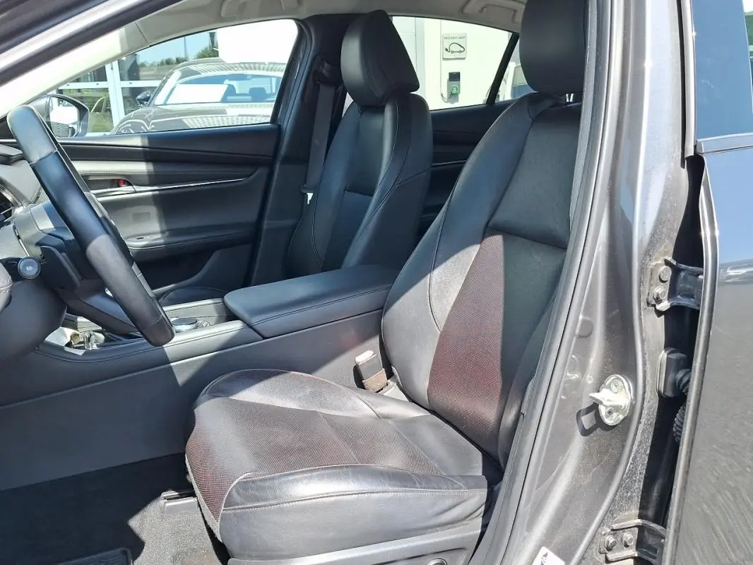 Vue intérieure côté conducteur de la Mazda3 gris 2020, sièges en cuir noir et volant multifonctions visible.