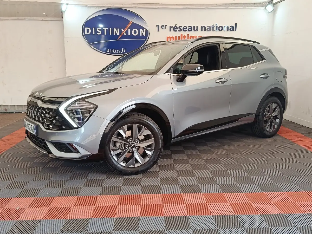 KIA Sportage gris clair vue 3/4 avant droit, avec calandre distinctive et rétroviseurs électriques ton caisse.
