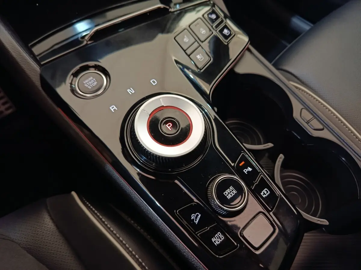 Gros plan sur la console centrale noire brillante du Kia Sportage 2022 avec sélecteur rotatif et boutons de contrôle.