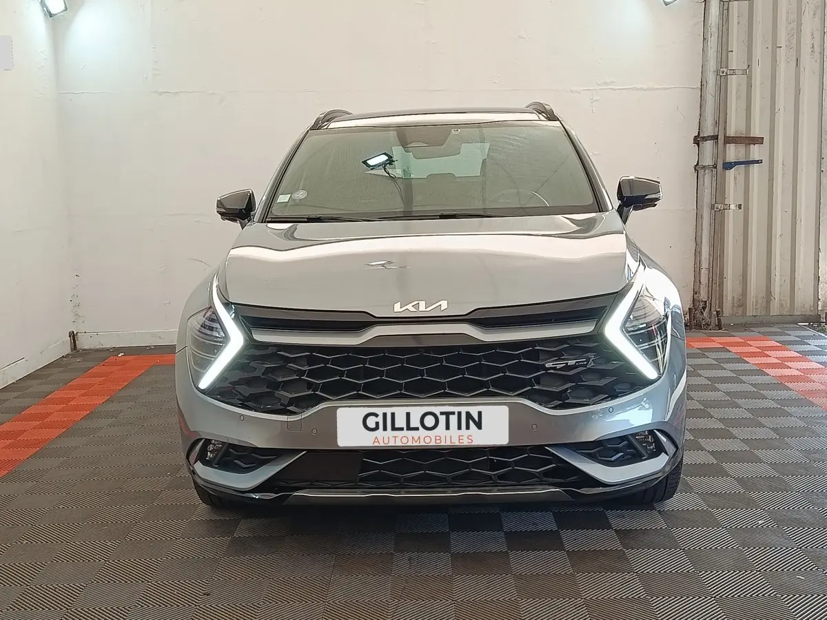 Vue frontale d'un KIA SPORTAGE gris clair 2022 avec feux LED en forme de flèche et calandre noire hexagonale.