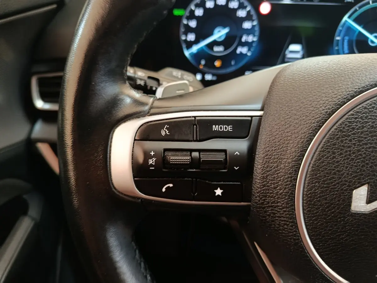 Gros plan sur les commandes gauche du volant cuir noir du Kia Sportage 2022 avec tableau de bord digital en arrière-plan.