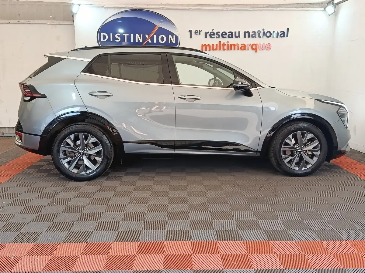 Profil droit d'un KIA SPORTAGE gris clair 2022 avec jantes alliage et rétroviseurs électriques dans un showroom.