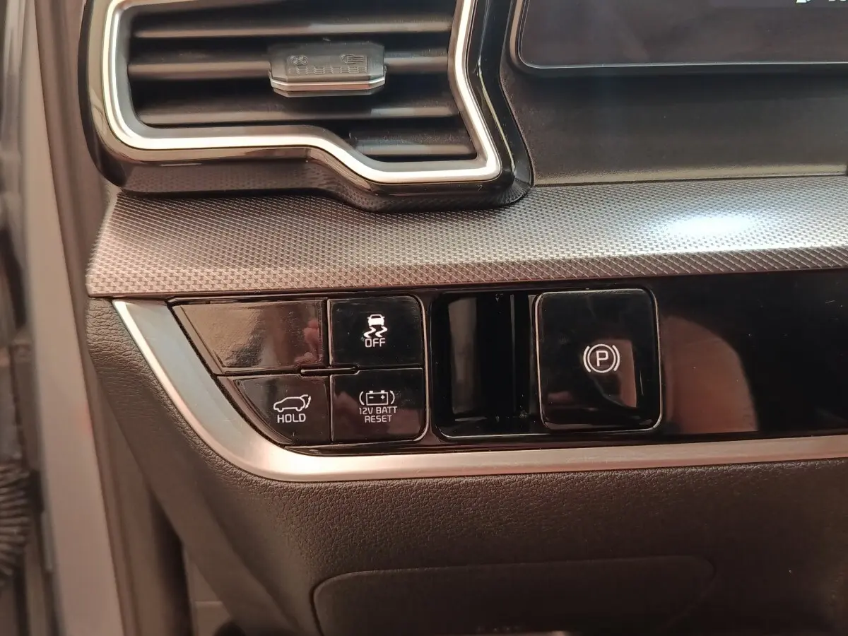 Gros plan sur les commandes noires du tableau de bord du Kia Sportage gris clair, avec boutons de frein à main et maintien de frein.