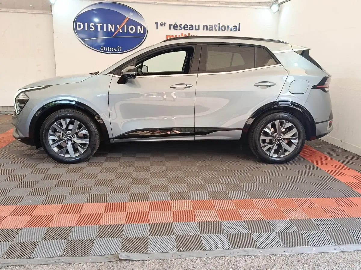 Vue latérale droite d'un KIA Sportage gris clair 2022 avec jantes alliage et protections noires sur passages de roues.