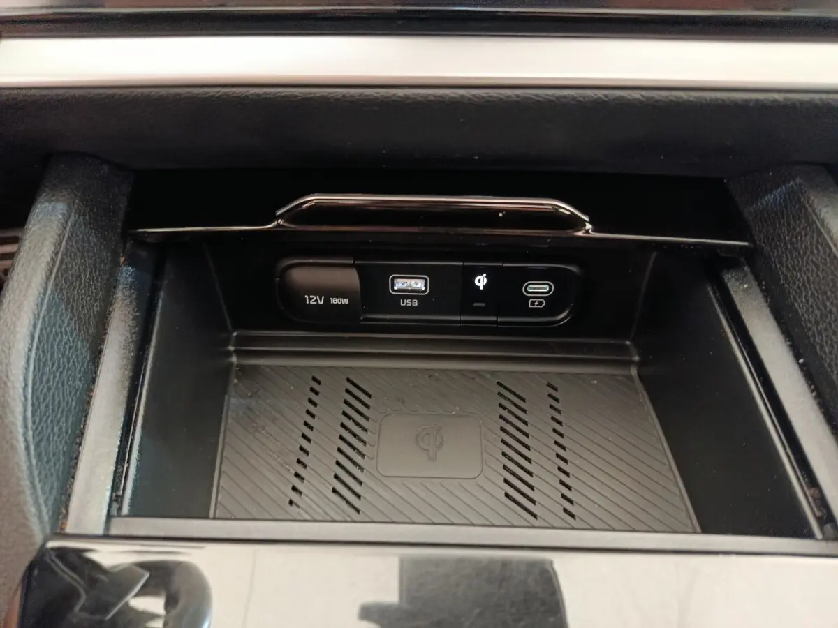Gros plan sur la zone de recharge sans fil et ports USB 12V du Kia Sportage gris clair 2022, intérieur noir.