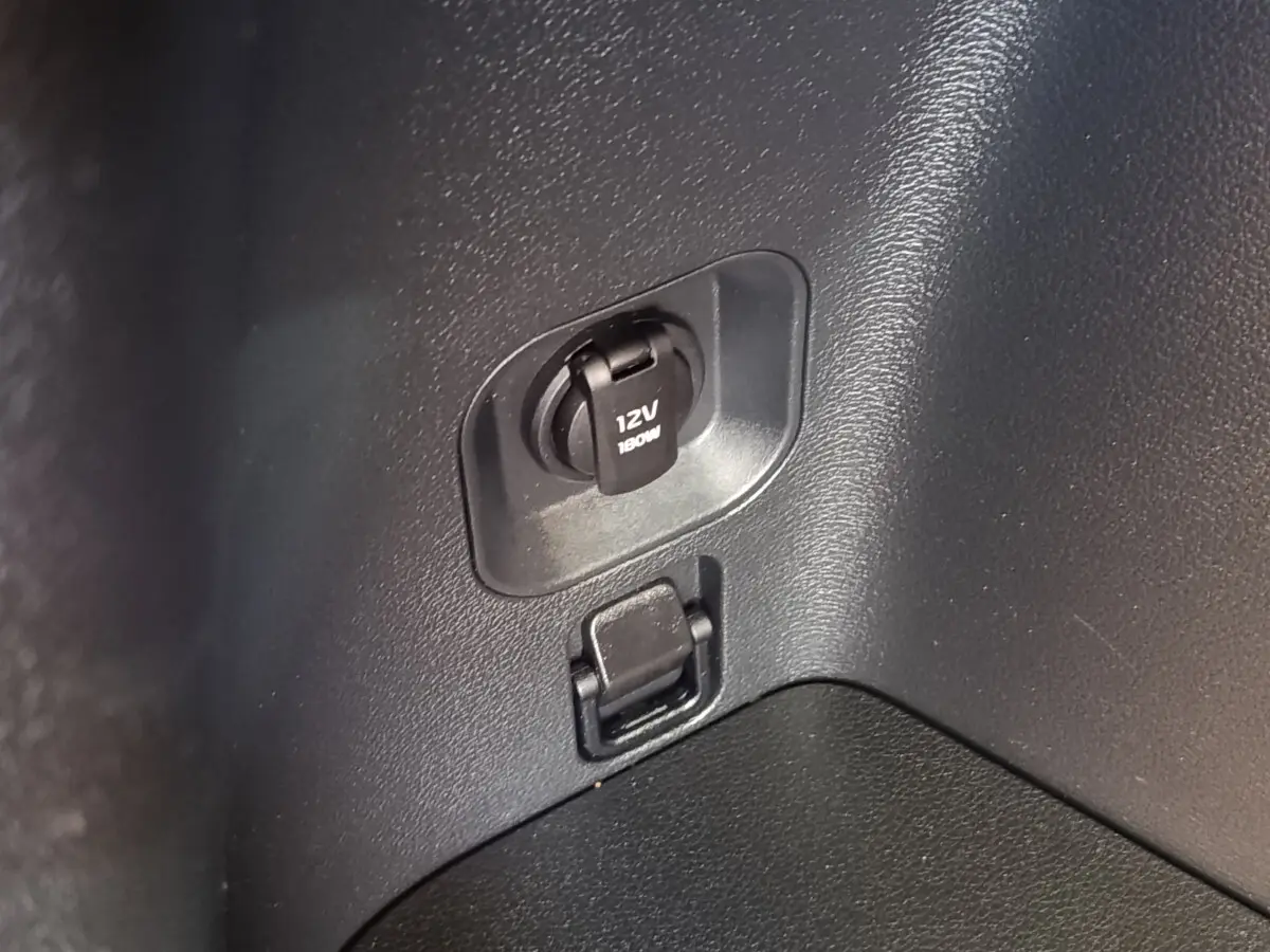 Prise 12V et port USB dans le coffre du Kia Sportage gris clair, vue rapprochée du panneau latéral intérieur.