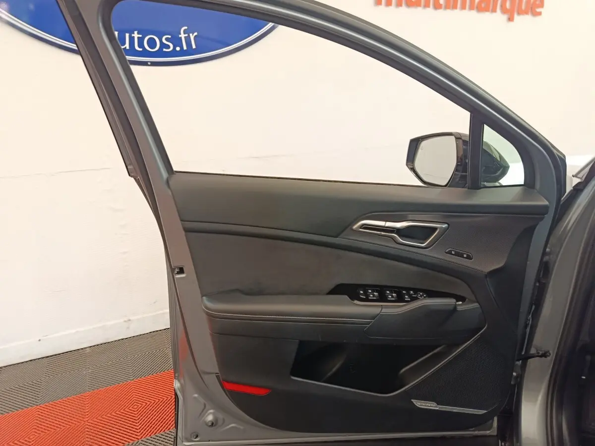 Vue intérieure de la porte avant gauche gris clair du Kia Sportage 2022 avec commandes électriques et insert décoratif noir.