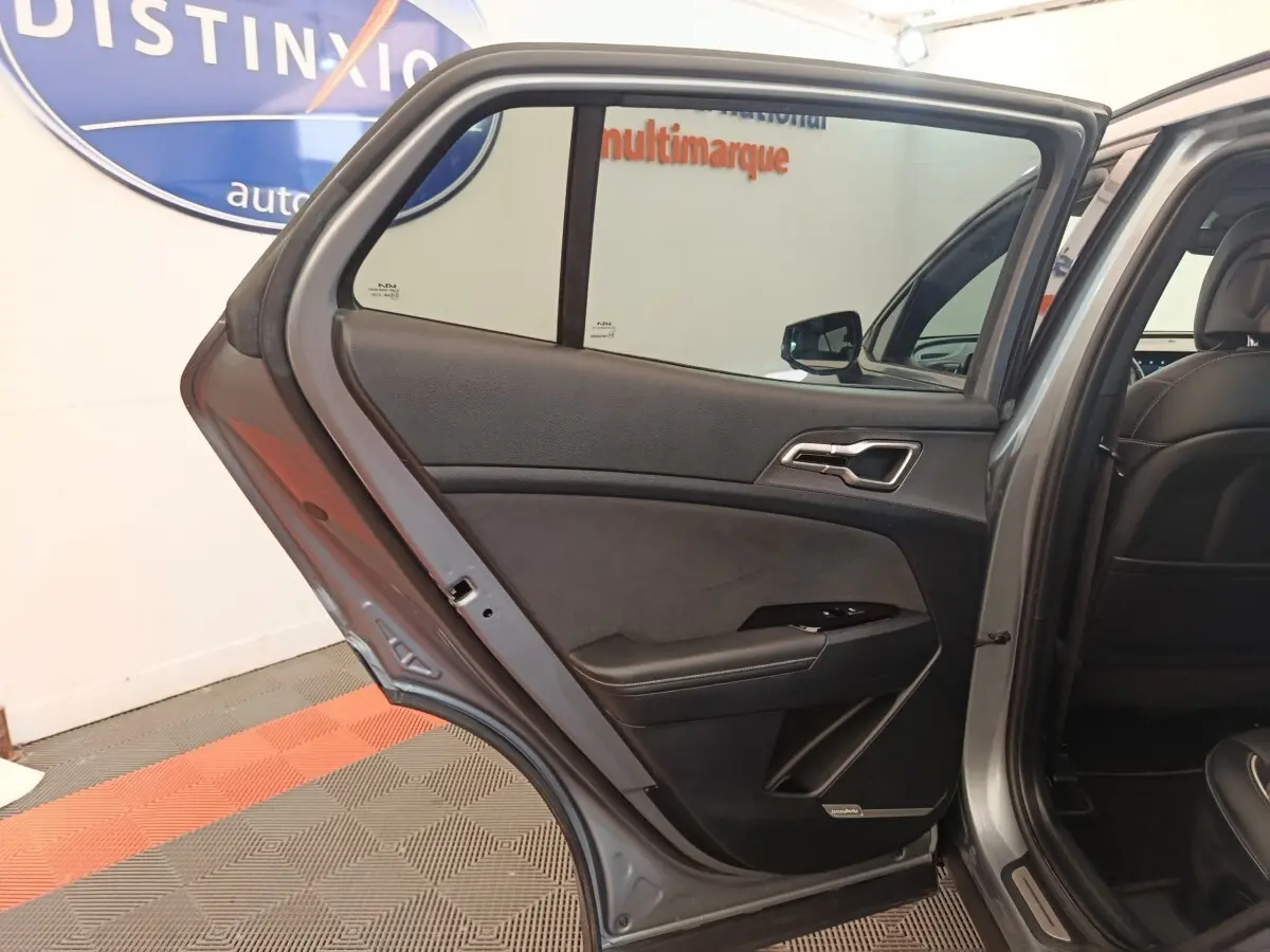 Vue intérieure côté gauche de la porte arrière ouverte d'un KIA Sportage gris clair avec garniture noire et détails chromés.