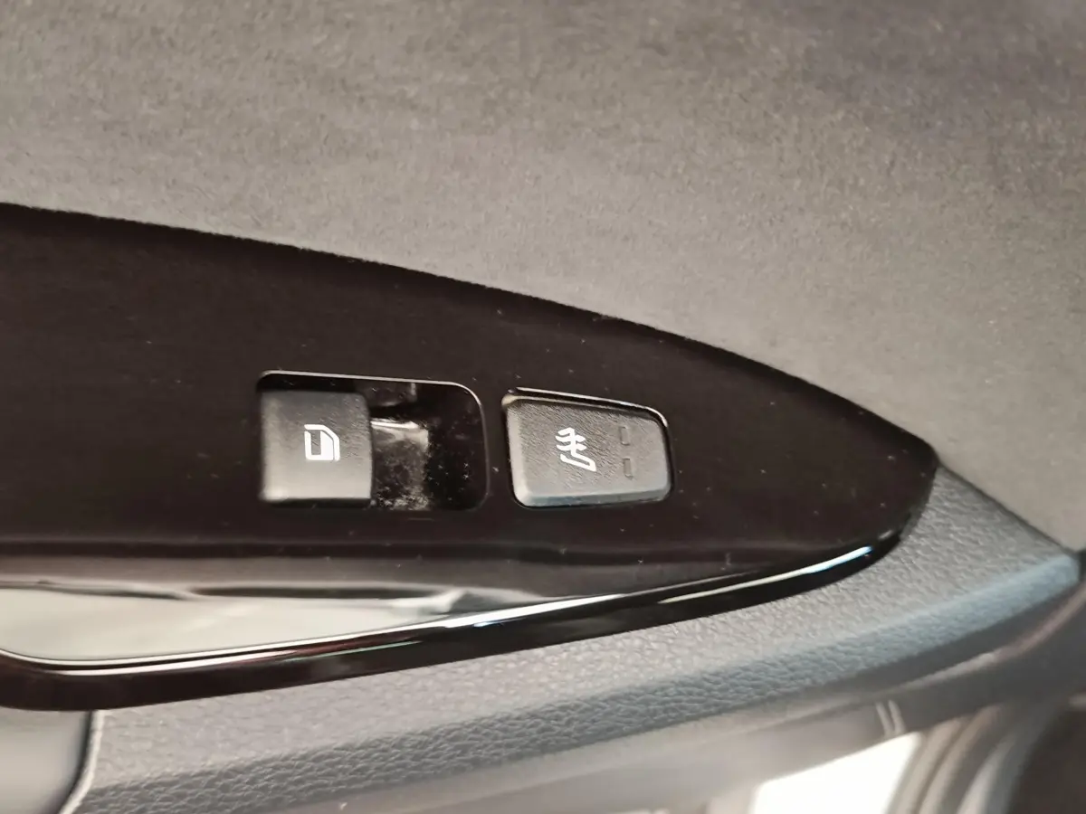 Gros plan sur les boutons de commande de verrouillage et de chauffage des sièges sur la porte intérieure noire d’un Kia Sportage gris clair.
