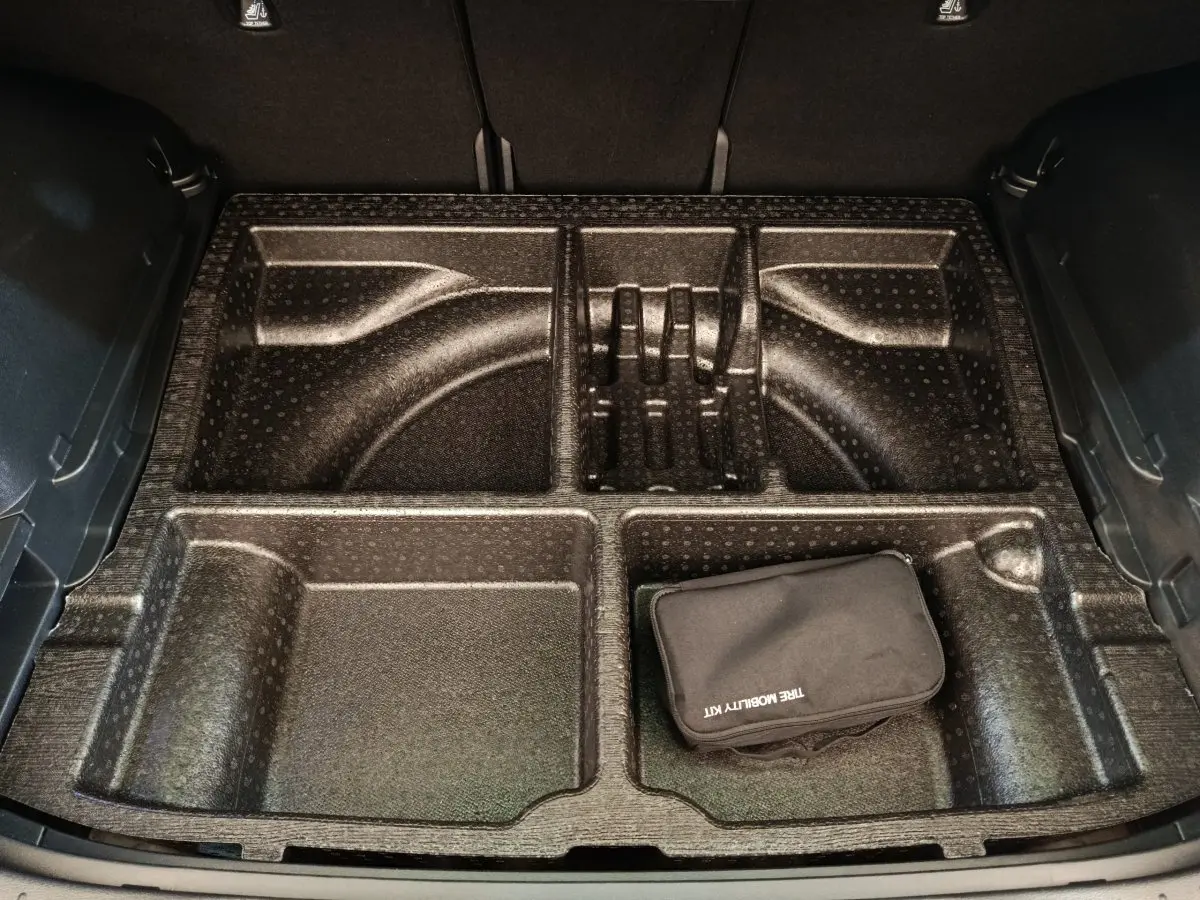 Coffre ouvert d’un Kia Sportage gris clair, vue plongeante sur le rangement compartimenté avec trousse de mobilité noire.