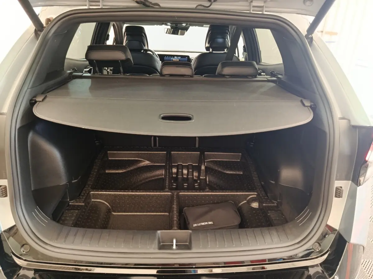 Coffre ouvert d’un KIA Sportage gris clair vu de l’arrière, avec cache-bagages et compartiments de rangement visibles.