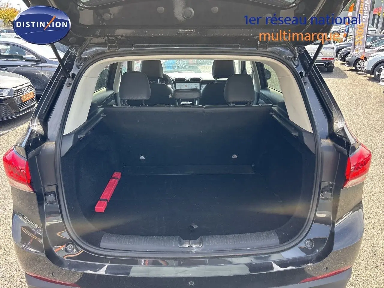 Coffre ouvert vu de l'arrière d'un MG MOTOR ZS 1.5L HYBRID+ 197CH LUXURY noir Pebble Black Metal, intérieur spacieux avec triangle de sécurité rouge.