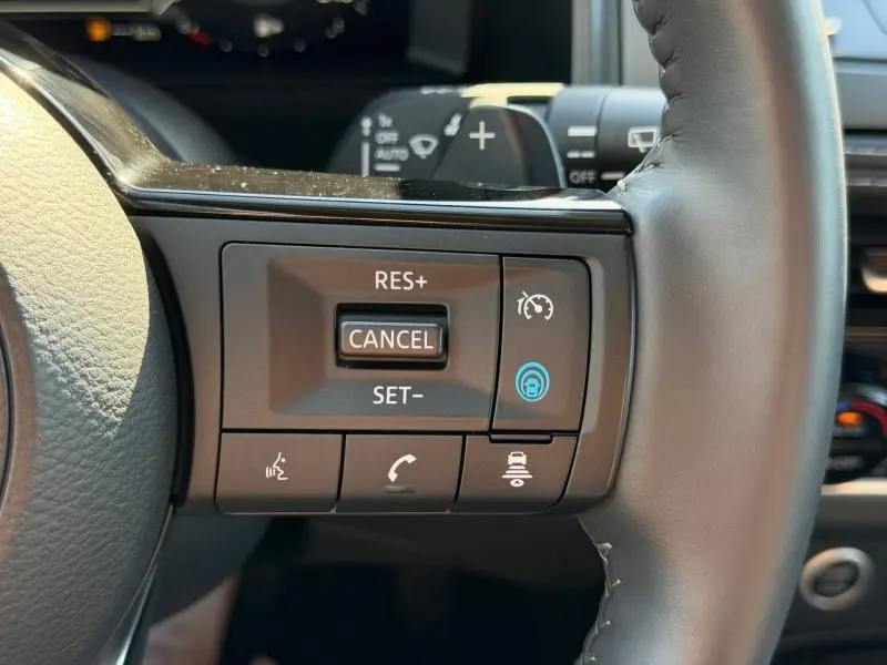 Gros plan sur les commandes du régulateur de vitesse au volant cuir du Nissan Qashqai noir Kuro Métallisé 2025.