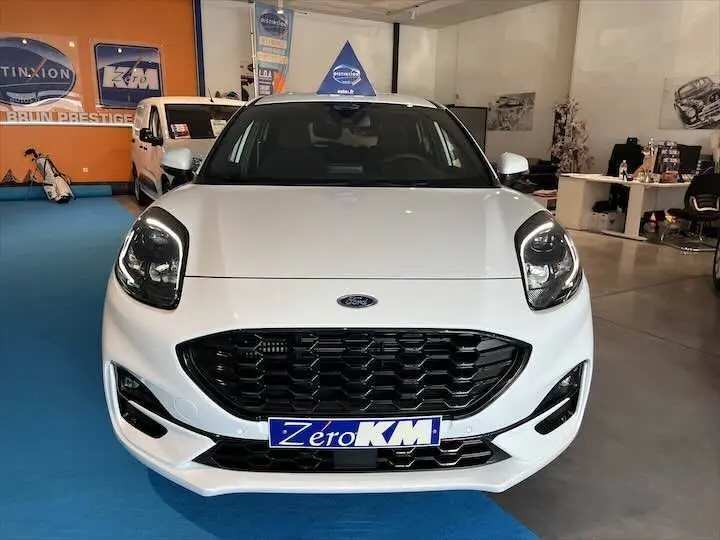 Vue frontale d'une Ford Puma blanc glacier en showroom avec calandre noire et plaque "Zero KM" visible.