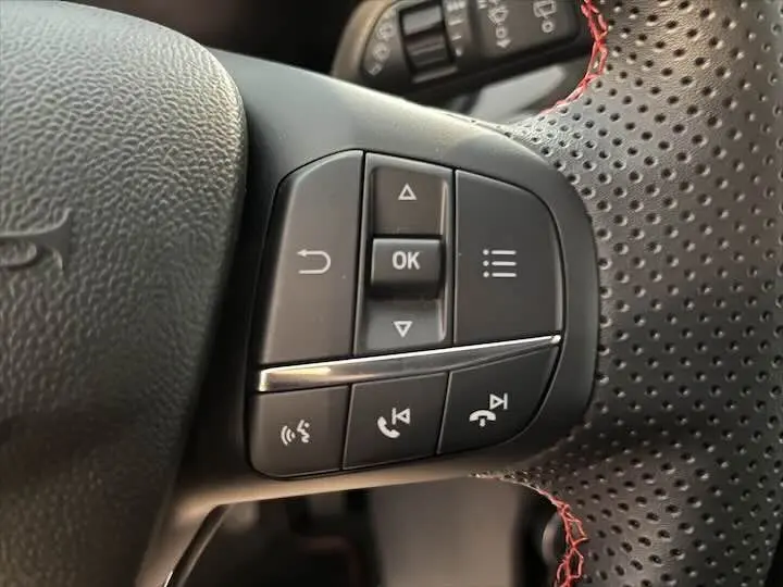 Gros plan sur les commandes multifonctions à droite du volant perforé avec surpiqûres rouges d'une Ford Puma blanc glacier 2022.