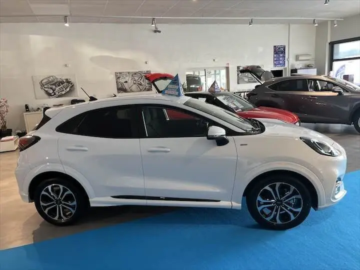 Ford Puma blanc glacier vu de profil côté gauche dans un showroom avec plusieurs autres véhicules en arrière-plan.