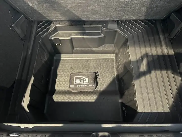 Coffre ouvert en vue plongeante du Ford Puma blanc glacier, mettant en valeur le rangement sous plancher avec trousse de secours.