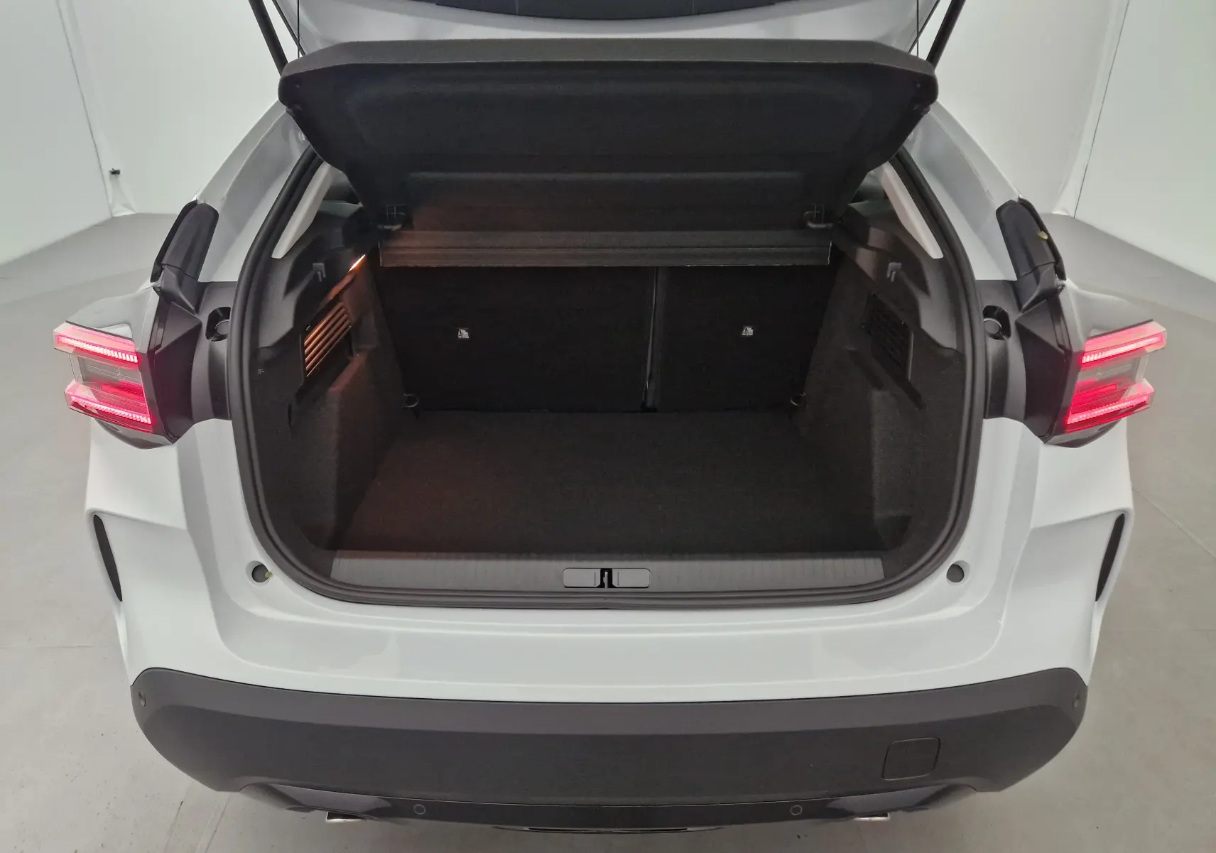 Coffre ouvert vu de l'arrière d'une Citroën C4 1.2 Hybrid 136 blanc Okenite avec feux arrière allumés.