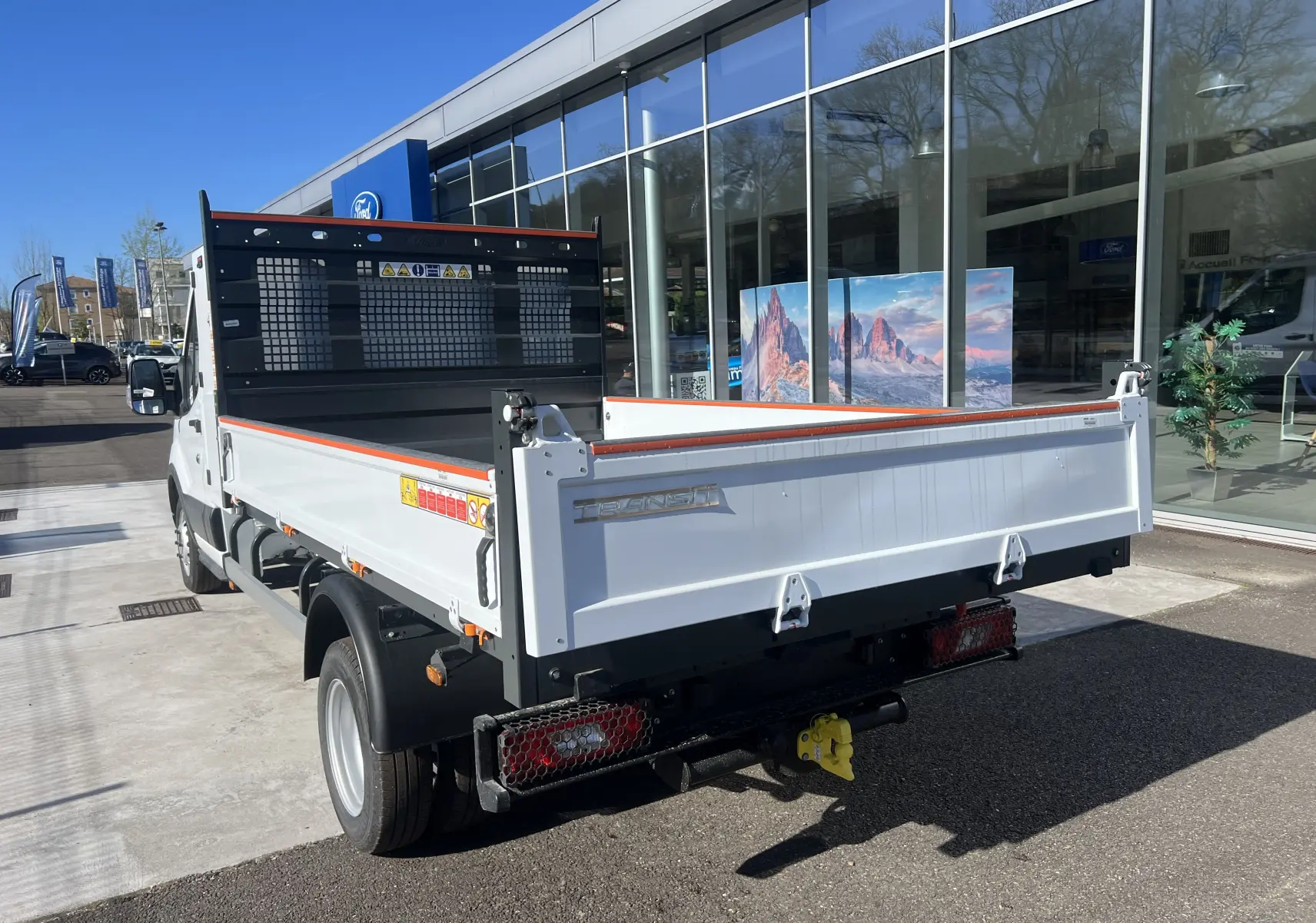 Vue 3/4 arrière droite d’un Ford Transit Chassis Cabine blanc avec benne et coffre, roues jumelées et attelage visible.