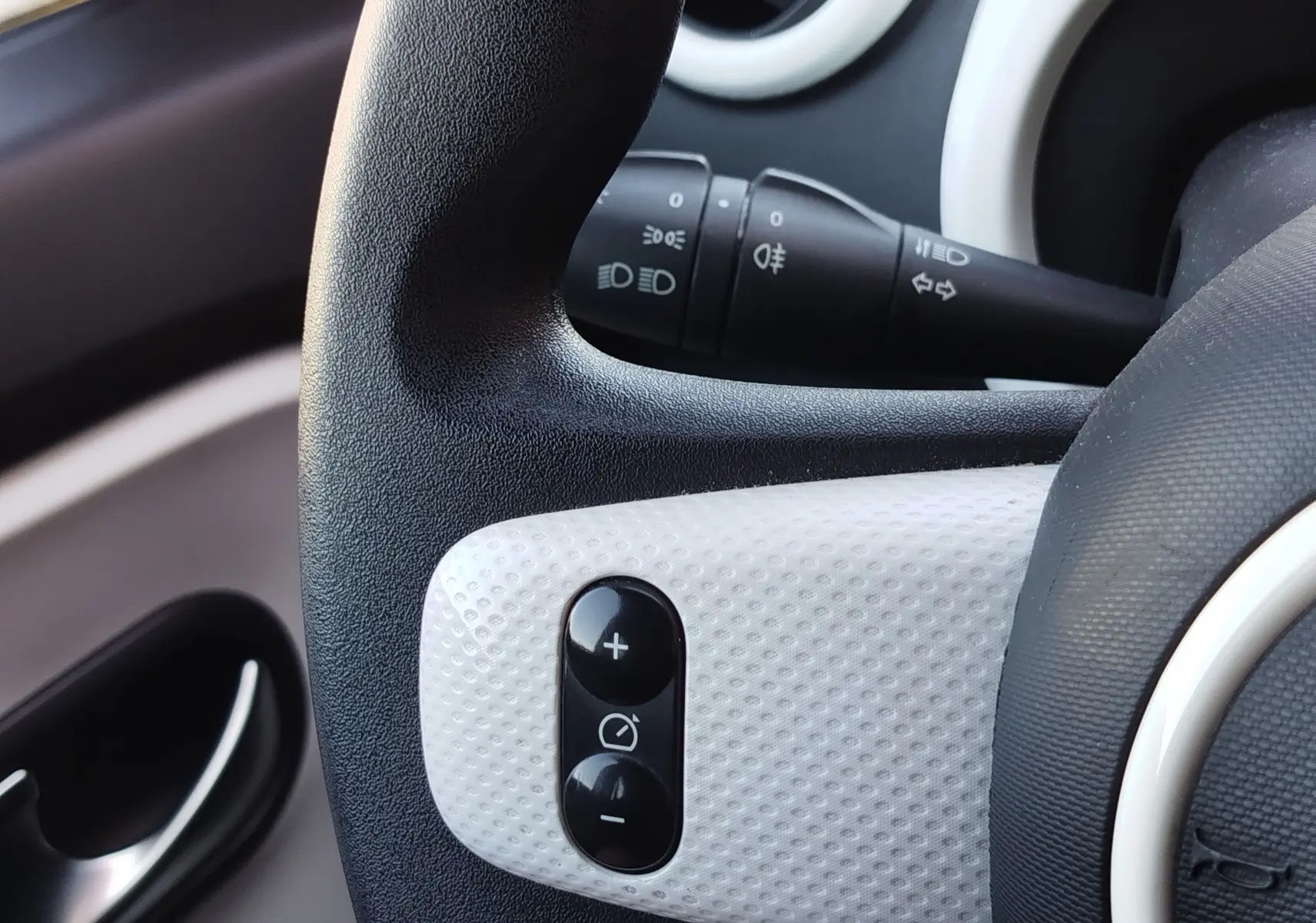 Gros plan sur la commande de régulateur de vitesse sur le volant noir et blanc d'une Renault Twingo Blanc Cristal 2016.