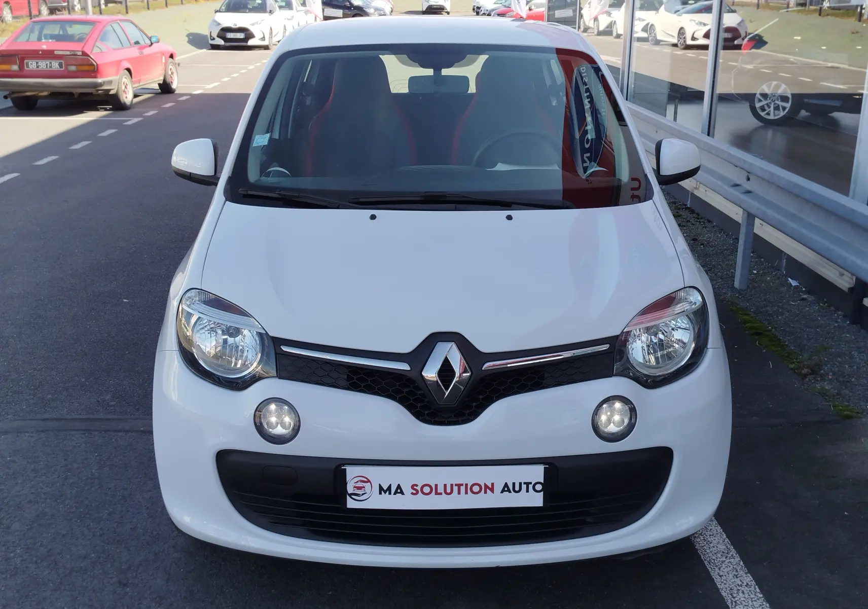 Vue avant d'une Renault Twingo blanche Cristal 2016 avec phares allumés et logo Renault bien visible.