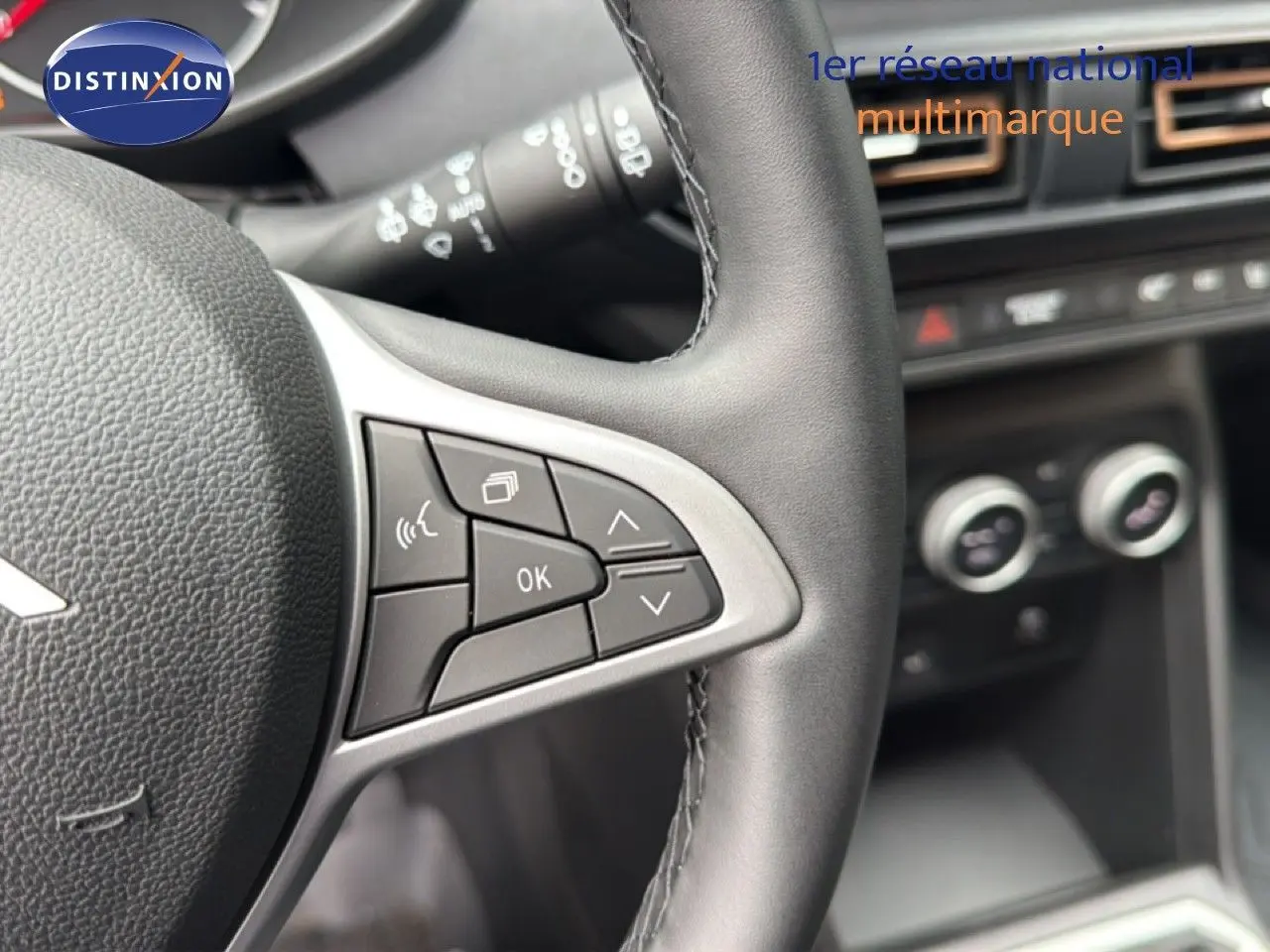 Gros plan sur le volant en cuir noir avec commandes intégrées, tableau de bord et commandes de climatisation floues en arrière-plan.