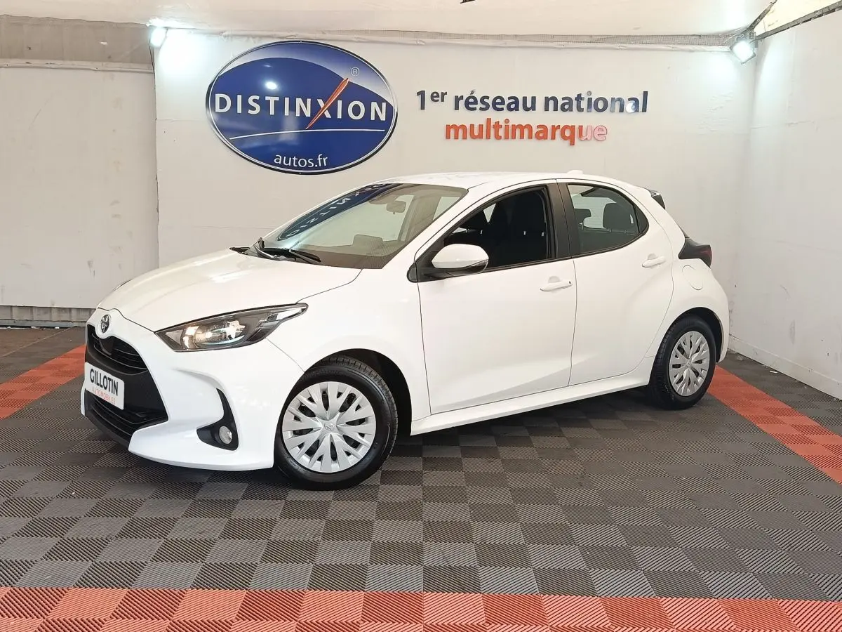 Toyota Yaris hybride blanche vue de profil avant droit dans un showroom avec logo Distinxion en arrière-plan.