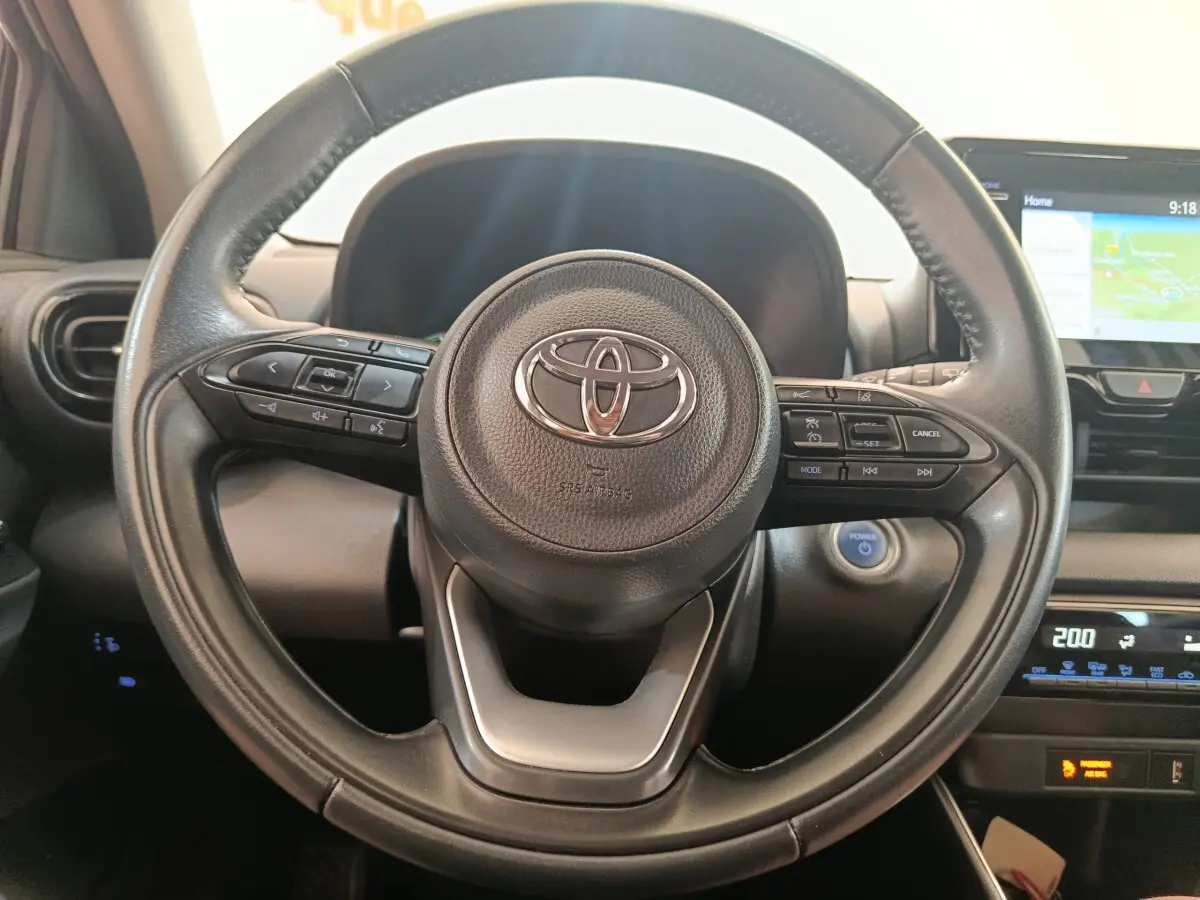 Vue rapprochée du volant cuir multifonctions noir de la Toyota Yaris Hybride 116h avec tableau de bord et écran tactile visibles.