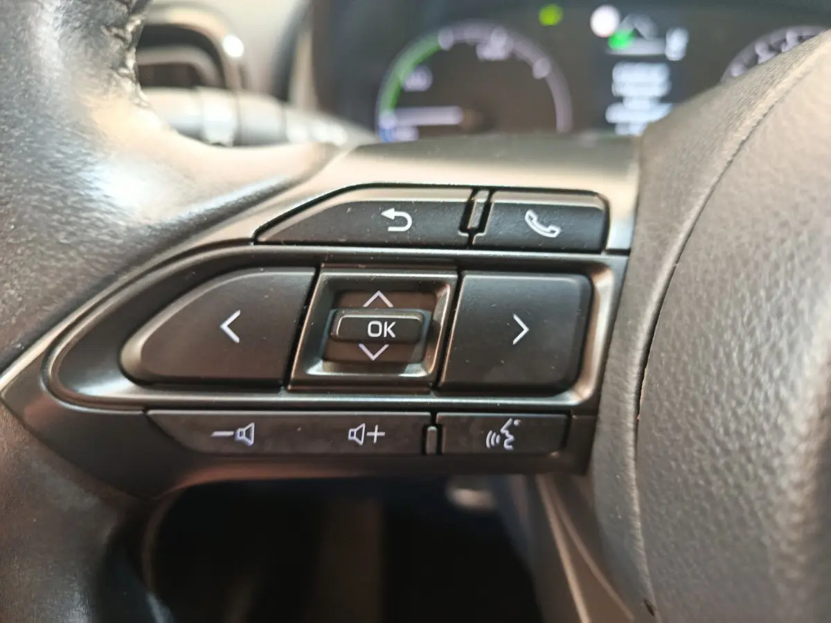 Gros plan sur les commandes multifonctions noires du volant cuir côté gauche de la Toyota Yaris hybride blanche 2022.