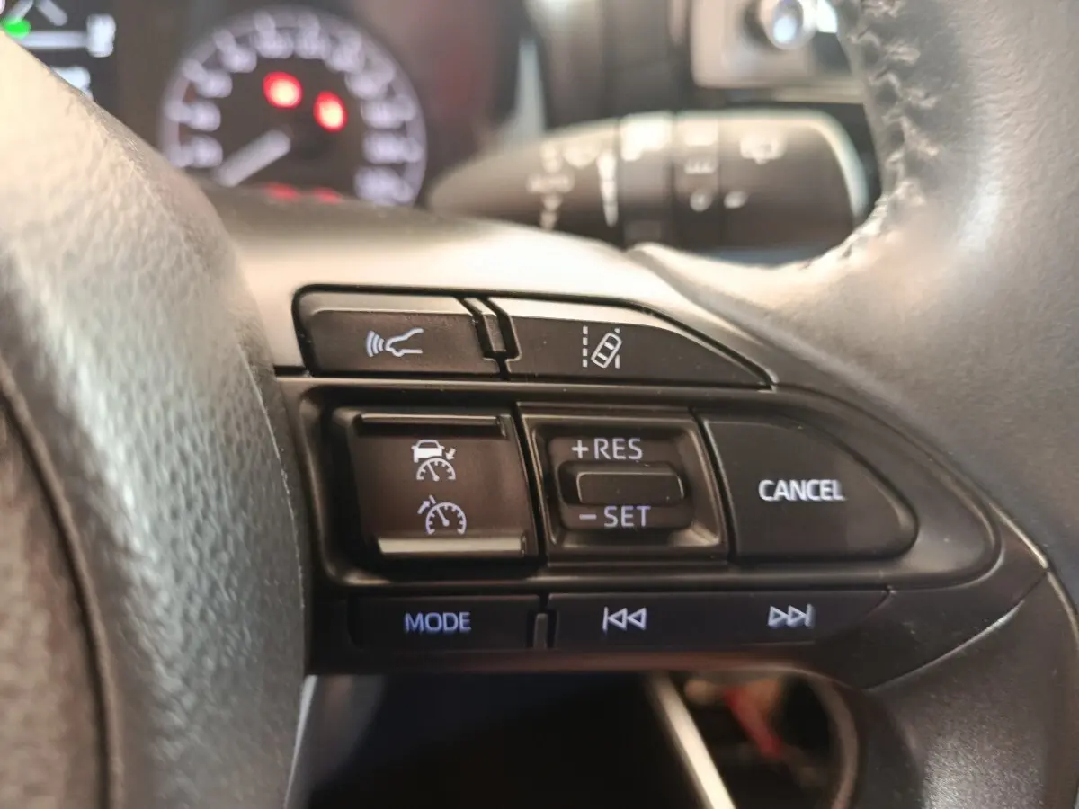 Gros plan sur les commandes du volant cuir multifonctions de la Toyota Yaris hybride 2022, boutons noirs avec symboles blancs.