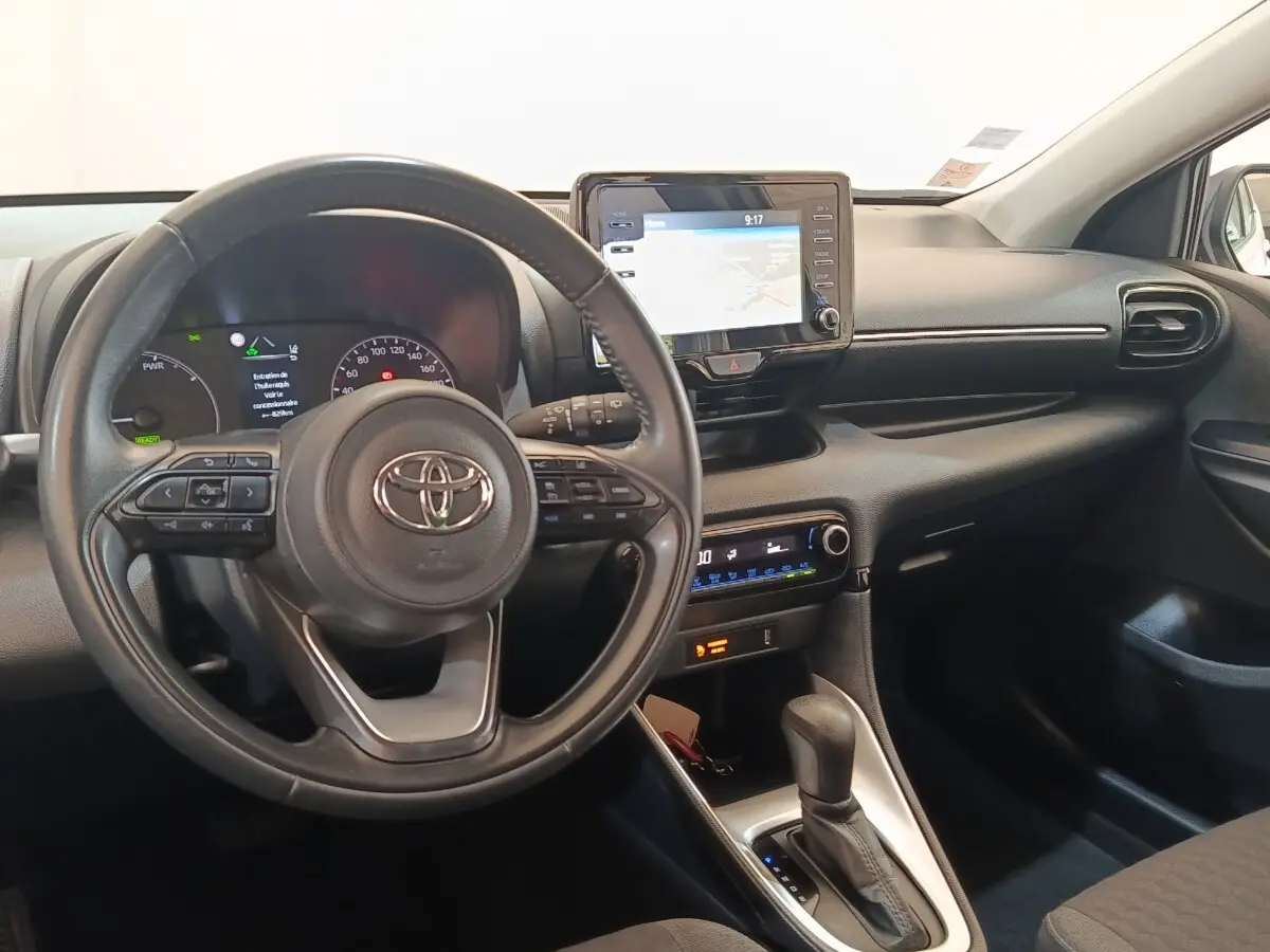 Vue intérieure avant de la Toyota Yaris hybride blanche 2022, volant cuir multifonctions et écran tactile de navigation.
