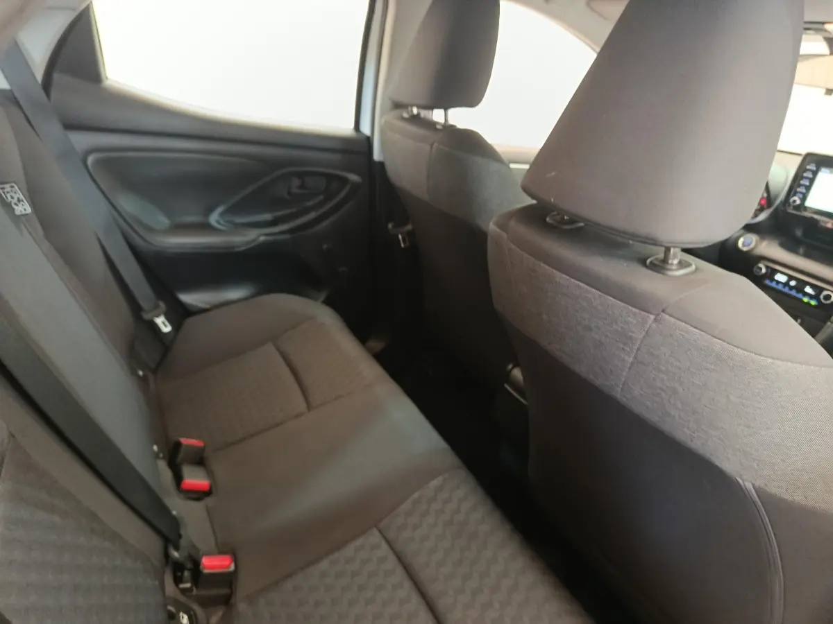 Vue intérieure arrière côté gauche de la Toyota Yaris hybride 2022 avec sièges tissu gris foncé et ceintures de sécurité.