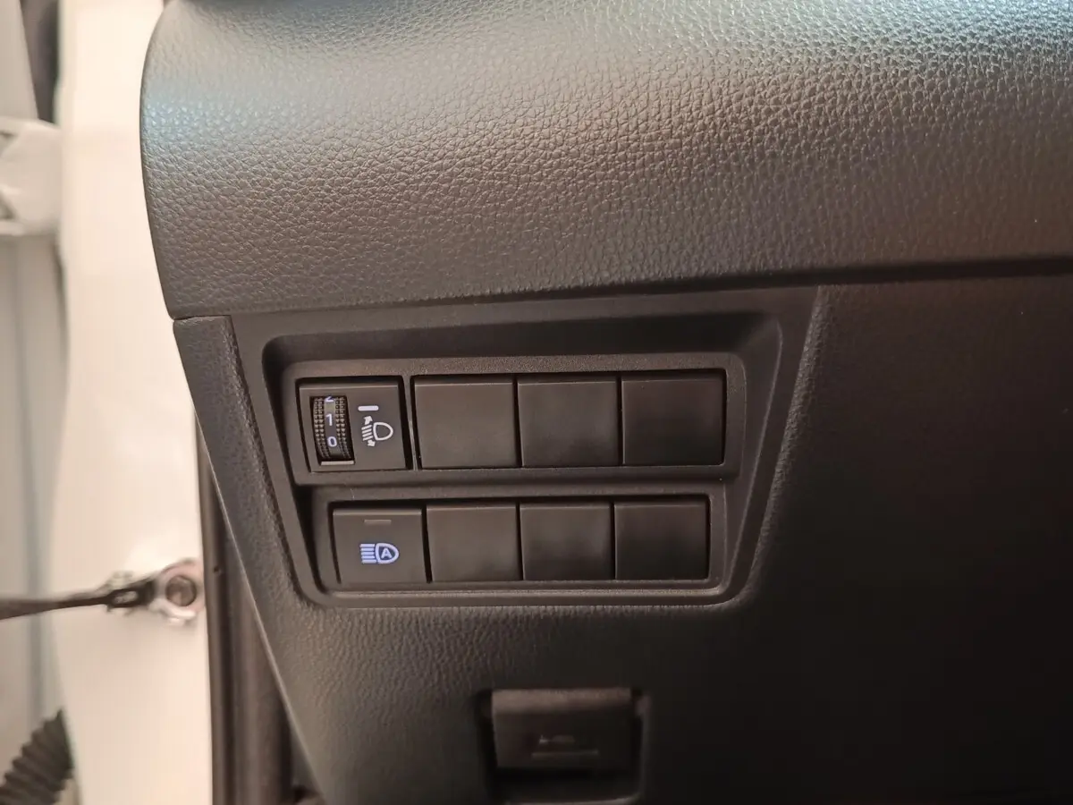 Détail intérieur montrant les commandes de réglage des phares sur la Toyota Yaris blanche hybride 2022.