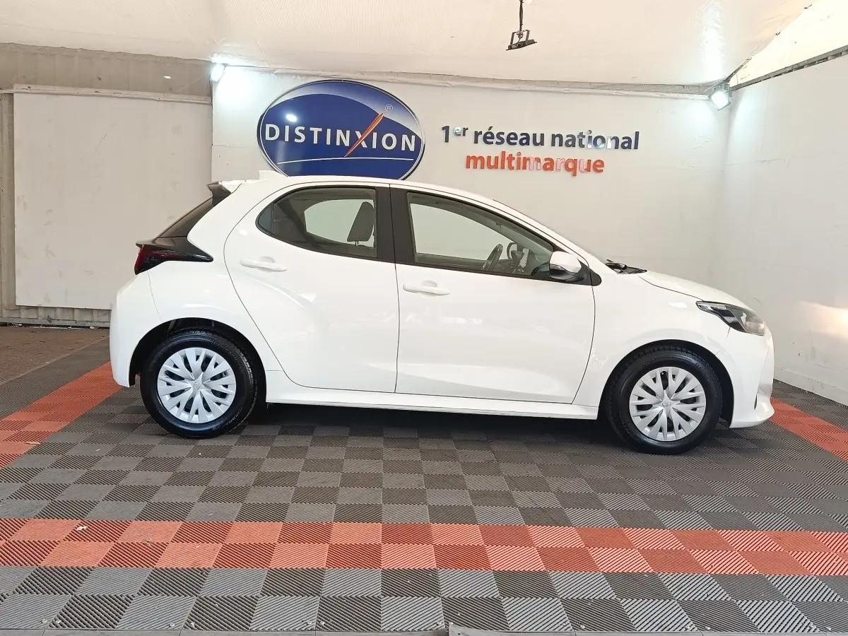 Profil droit de la Toyota Yaris hybride blanche 2022, avec jantes pleines et toit noir contrastant visible en arrière-plan.
