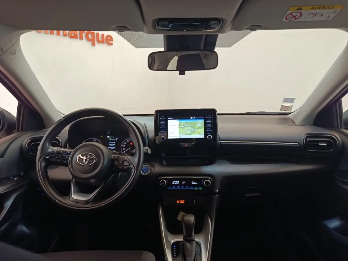 Vue intérieure avant du tableau de bord noir d'une Toyota Yaris hybride 2022 avec écran tactile central et volant cuir multifonctions.