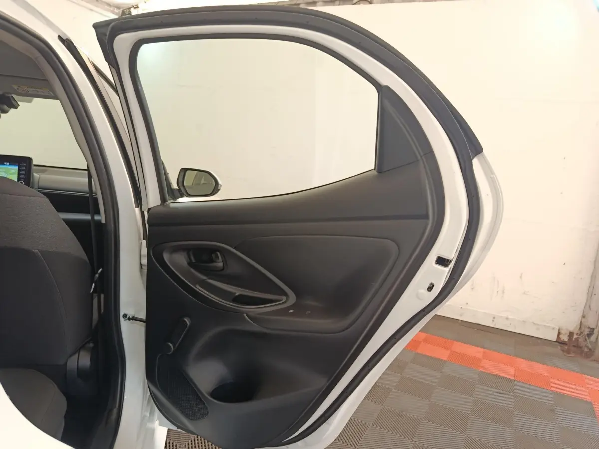 Vue intérieure de la porte arrière droite ouverte d'une Toyota Yaris hybride blanche, montrant la garniture noire.