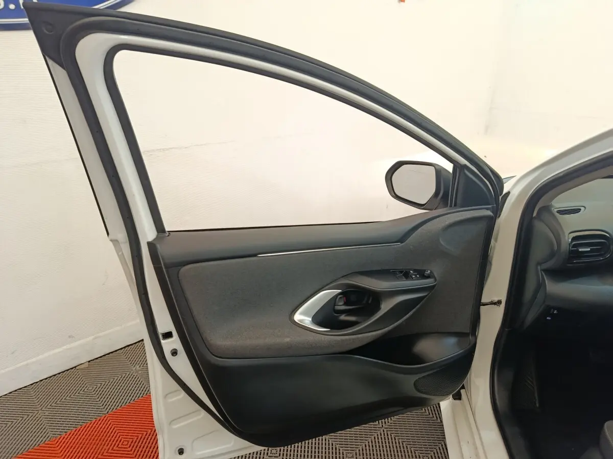 Vue intérieure de la porte avant gauche ouverte d’une Toyota Yaris blanche, montrant la garniture noire et grise.